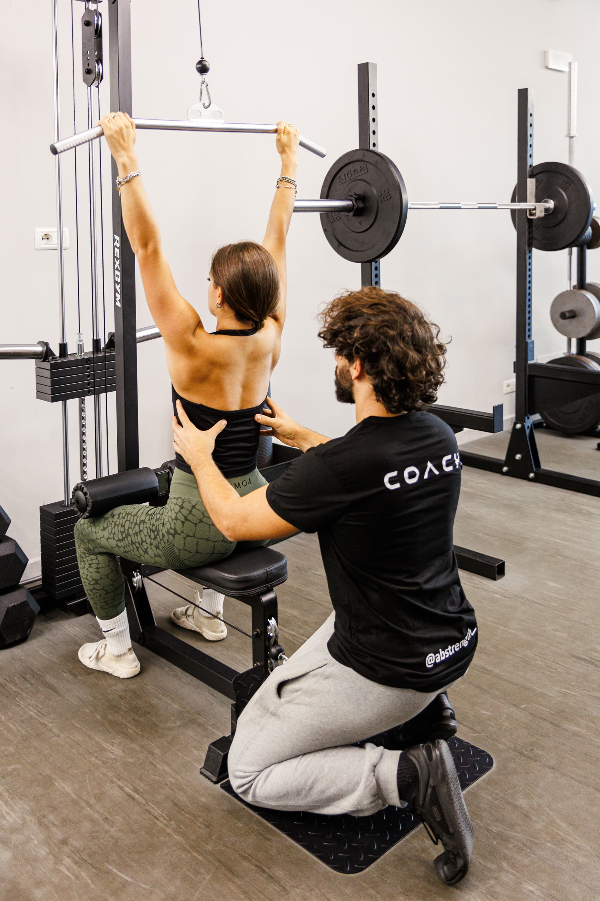 Alessandro, in ginocchio, corregge la schiena di un'atleta alla lat machine